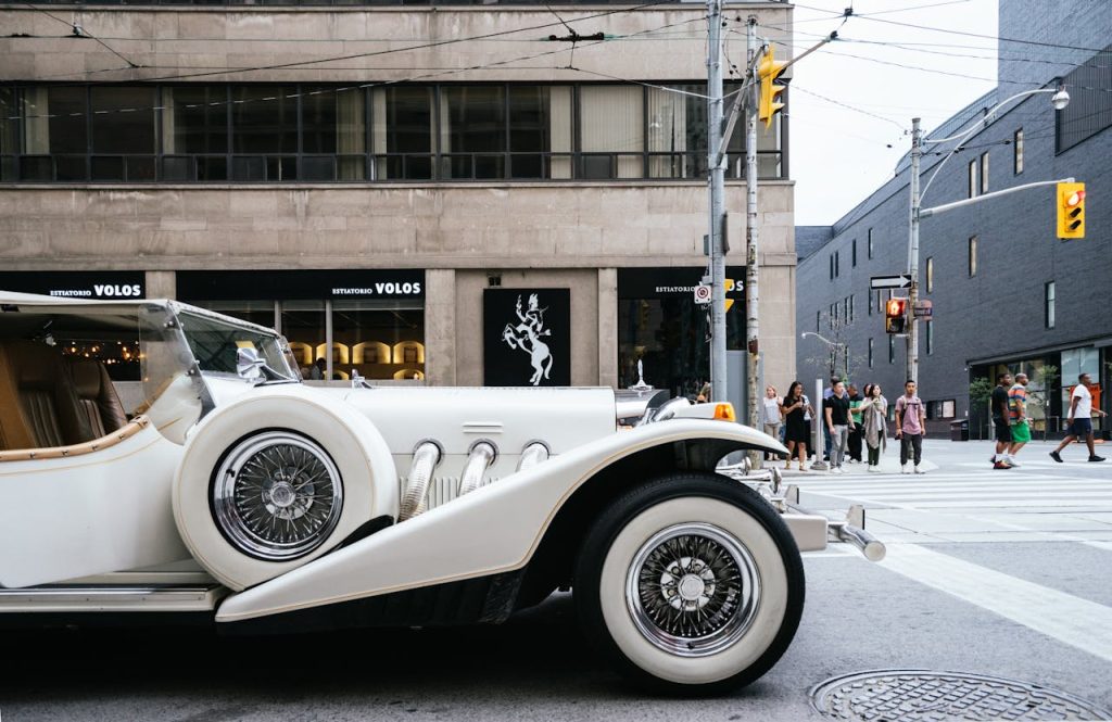 Vintage white limousine parked on an urban street corner with pedestrians in the background.
