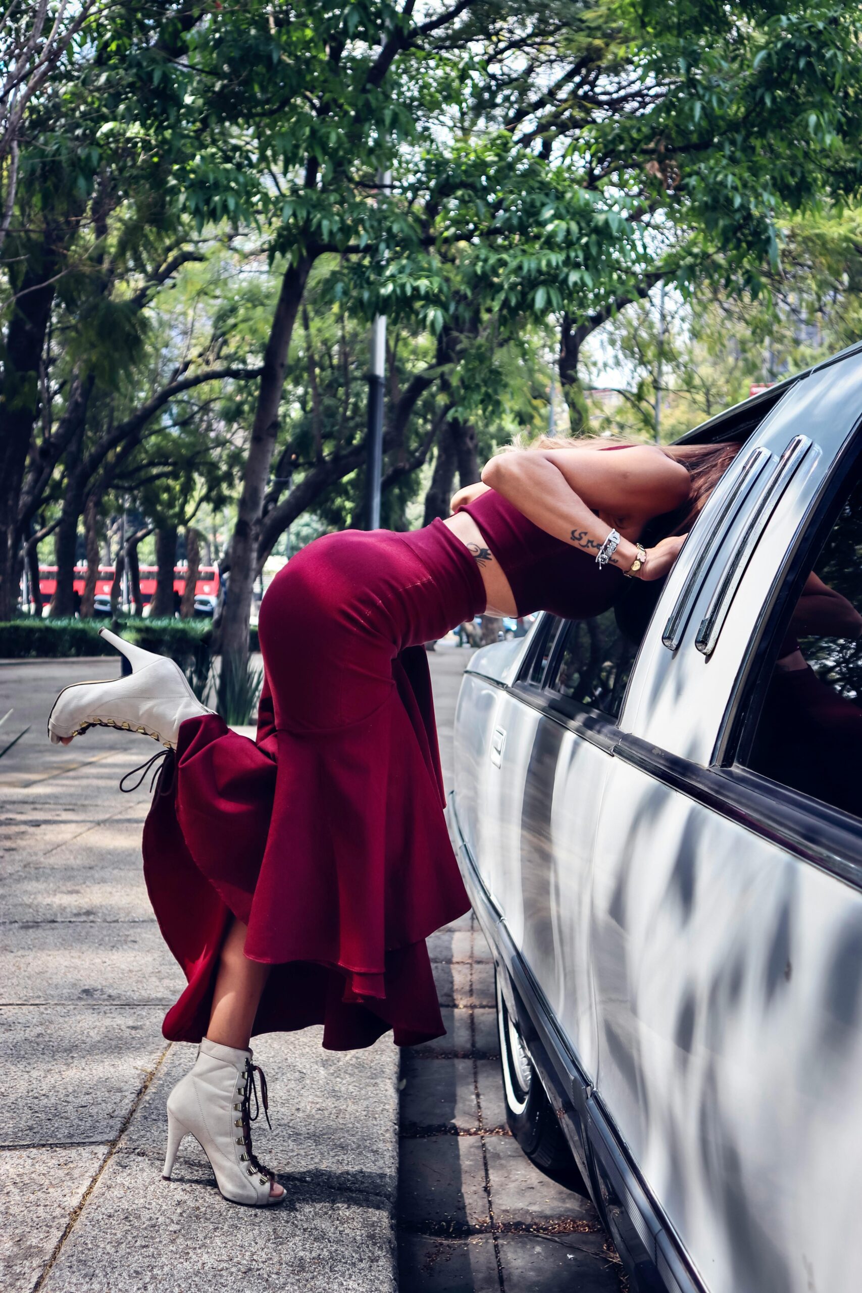 Stylish woman in red dress stepping into a limousine on a sunny day.